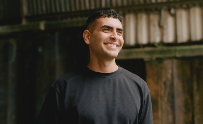 Sammy Virji poses in a black top in front of a dishevelled backdrop