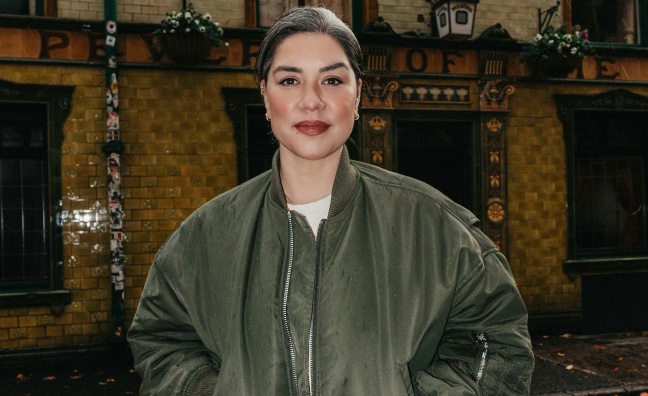 Stacey Tang wears a dark green bomber jacket stood in front of Manchester pub, The Peveril of the Peak